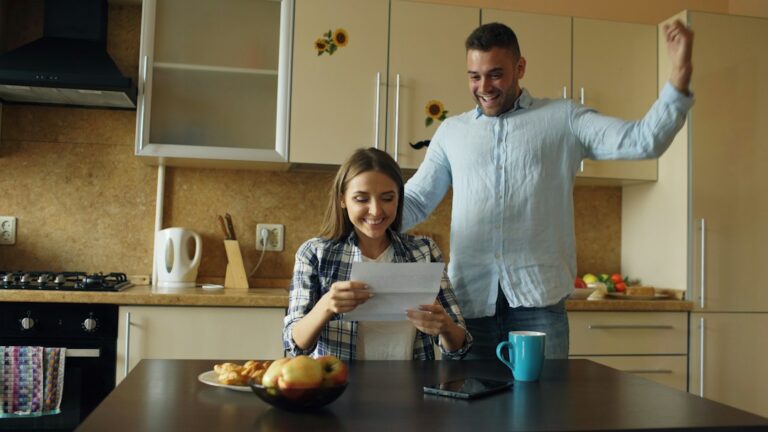 A couple reviews insurance documents beside a laptop, calculator, keys, and a home inventory notebook.